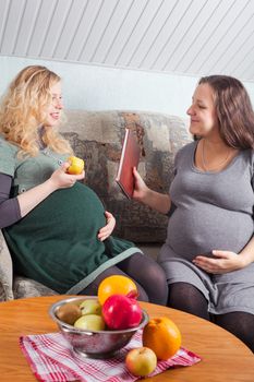 Two pregnant women eat fruits and discuss pregnancy and preparation to parenting