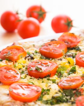 Pizza with cherry tomatoes and dry basil on the ceramic white plate closeup