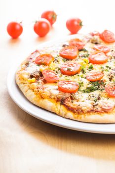 Pizza with cherry tomatoes and dry basil on the ceramic white plate closeup