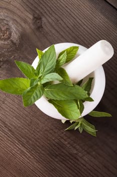 Fresh green mint in mortar on wood background closeup