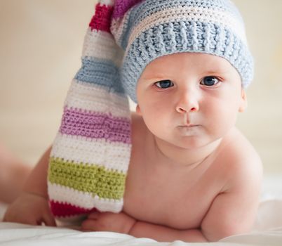 Baby in funny crochet hat lying on the bad