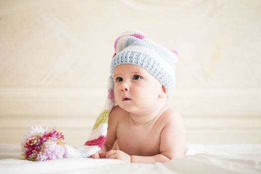 Five-month baby in crochet hat lies on the bed