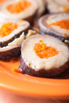 Herring rolls with carrot on orange plate closeup