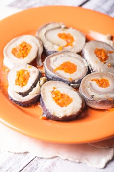 Herring rolls with carrot on orange plate closeup