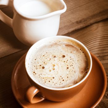 Coffee in brown cup and milk on wood background closeup