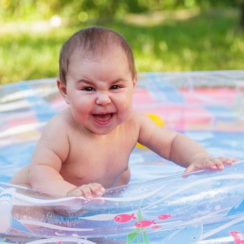 Cute baby in the inflatable pool on grass