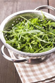 Fresh wet arugula in the colander on the table