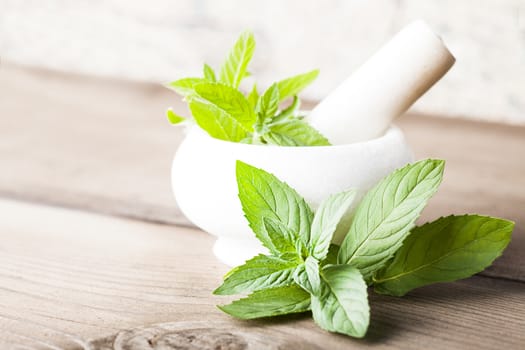 Fresh green mint in mortar on wood background closeup