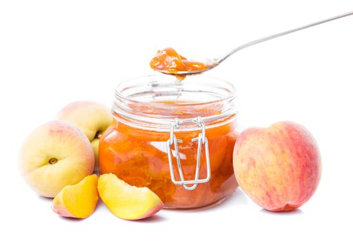 Tasty peach jam in glass jar with fruits over white