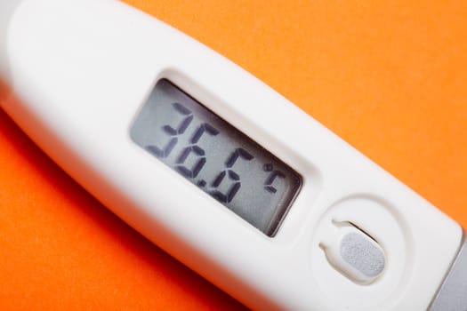 Electronic thermometer with 36,6 C closeup on the orange backgroun