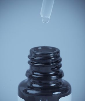 Glass bottle with pipette on blue background