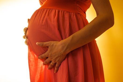 Abdomen of pregnant women in pink dress on the backlight