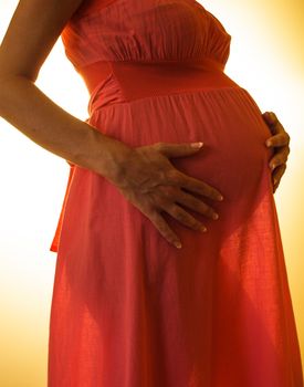 Abdomen of pregnant women in pink dress on the backlight