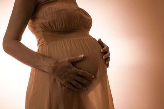 Abdomen of pregnant women in pink dress on the backlight