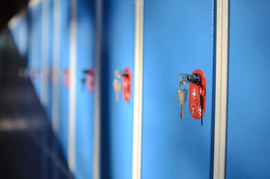 Blue metal cupboards in chamging room at swiming pool, with visible keys and red label.