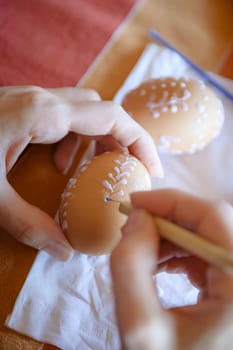 Traditional decorating of the easter eggs by the woman, visible woman's hands, in the background visible another easter egg, shallow DOF.