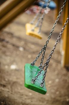 Abandoned autumn, fall playground, with green swings and yellow swings in the background, chain swings.