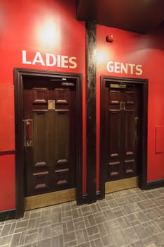 Entrance to the WC,  toilets in the restaurant, separate for ladies,women and gents,menon the red wall, dark brown door.