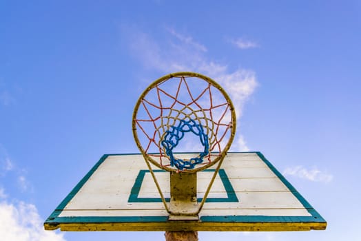 Old style basketball basket with the board, shot from bottom with visible blue sky in the background.