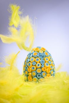 Funny, amusing and joyful photo of yellow and blue Easter egg lying in yellow feathers, visible feather falling down.