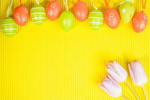 Easter arrangement on yellow background, visible orange and green  decorated eggs and pink tulips in right corner, space for text provided.
