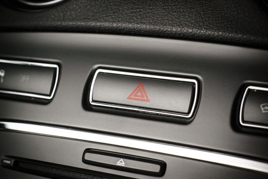 Button of vehicle, car hazard warning flashers button with visible red triangle, visible  fragment of control panel, visible red triangle emergency symbol.