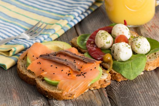 Delicious sandwiches for a healthy picnic with toppings of avocado, smoked salmon and anchovies on whole grain bread or baby spinach with mozzarella and chili pepper on a rustic table