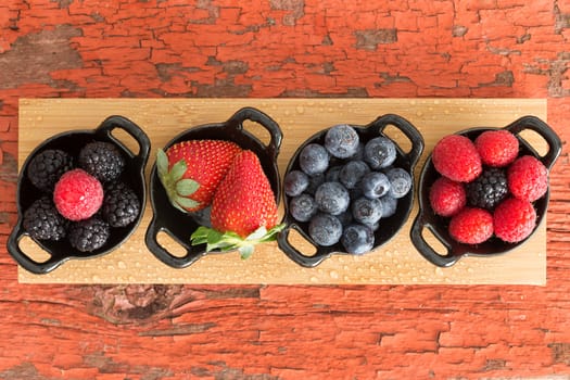 Assortment of ripe fresh autumn berries displayed on a wooden board in individual dishes with raspberries, blackberries, blueberries and raspberries on a grungy wooden table with peeling paint