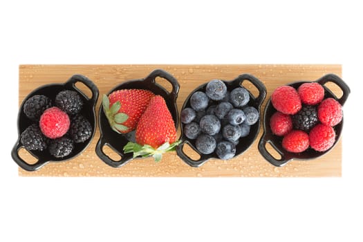 Healthy juicy autumn or fall strawberries, blueberries,. blackberries, and raspberries displayed in individual ceramic ramekins on a wooden board isolated on a white background, view from above