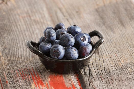 Healthy ripe autumn blueberries in a ceramic dish on an old rustic wooden picnic table for a delicious healthy snack