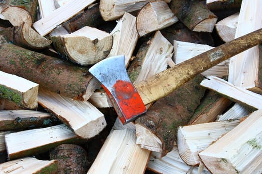 A pile of split firewood logs with an ax