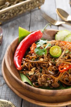Mee goreng mamak or mi goreng, Indonesian and Malaysian cuisine, spicy fried noodles with wooden dining table setting. Fresh hot with steamed smoke.