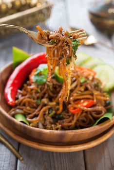 Indonesian and Malaysian cuisine, spicy fried noodles, mi goreng or mee goreng mamak with wooden dining table setting. Fresh hot with steamed smoke.