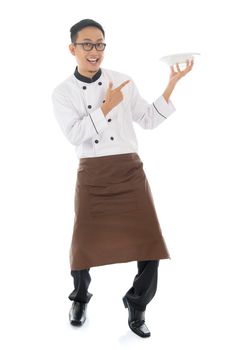 Full body Asian chef holding and pointing to an empty plate, standing isolated on white background.