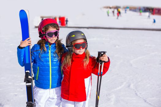 Kid girls sister in winter snow with ski equipment helmet goggles poles