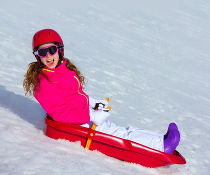 Kid girl playing sled in winter snow with helmet ang goggles