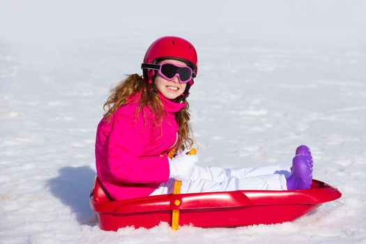 Kid girl playing sled in winter snow with helmet ang goggles