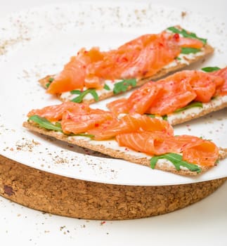 Salted salmon on crispy bread with cheese and arugula, closeup