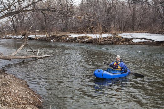 senior male paddling a packraft (one-person light raft used for expedition or adventure racing) on the Cache la Poudre River in Fort Collins, Colorado, winter or early spring