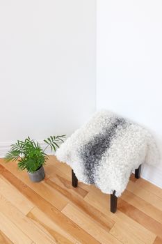 Home decor. Green plant and stool covered with sheepskin in the room corner.
