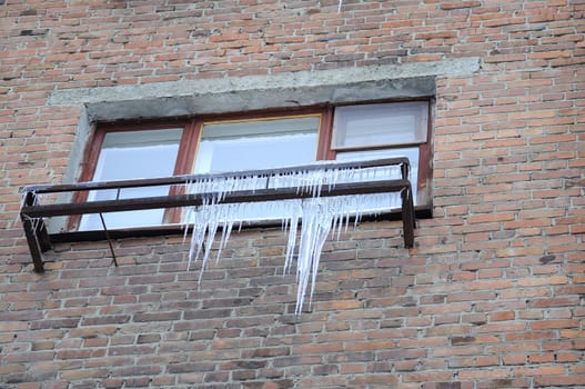 Big icicles at a window, against a brick wall