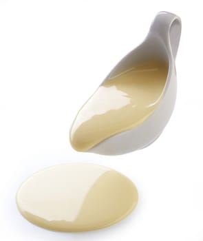 Isolated yellow condensed milk flowing from white sauce-boat