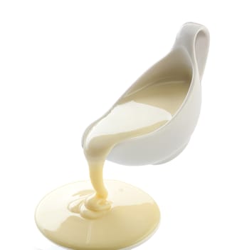 Isolated yellow condensed milk flowing from white sauce-boat