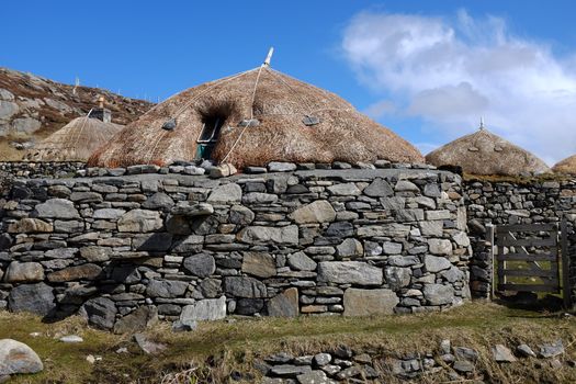 Traditional restoration of an historic building with a thatched roof and stone weights against a blue sky with cloud.