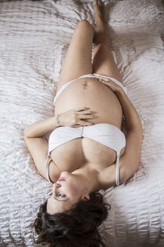 young pregnant woman lying on the bed, cheerful expectation, stomach