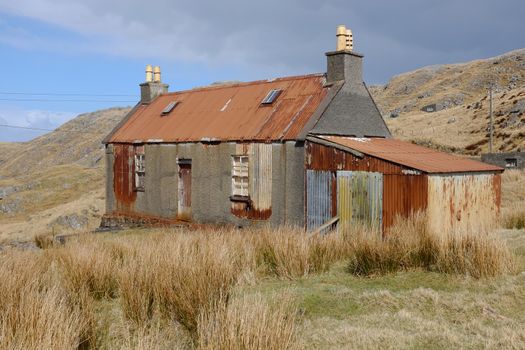 An old derelict building on moorland with tin corrugated roof and shed attached with partial render on the walls.