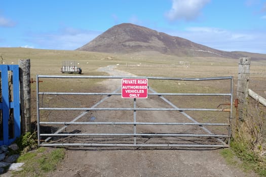 A closed gate with a red sign and the words 'PRIVATE ROAD AUTHORISED VEHICLES ONLY' written in white and a track leading into the distance with a hill against a blue sky.