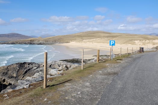 A sign with the parking symbol 'P' by a strip of tarmac overlooking the sea with a white sandy beach.