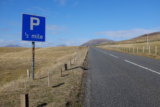 A blue square sign with the letters 'P 1/2 mile', parking in half a mile, next to a road leading to mountains in the distance.