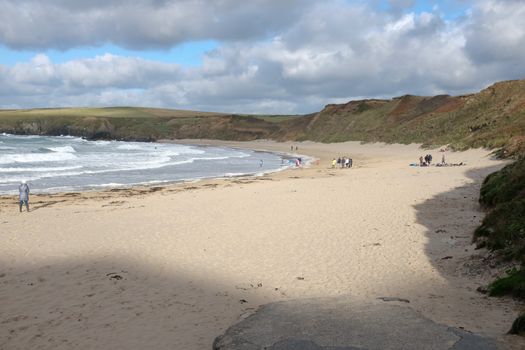 White sandy beach with people near the sea with waves, Whistling Sands, Porth Oer, on the Lleyn peninsular, North Wales, UK.